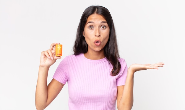 Young hispanic woman looking surprised and shocked, with jaw dropped holding an object and holding batteries