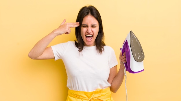 Young hispanic woman looking unhappy and stressed suicide gesture making gun sign clothes iron concept