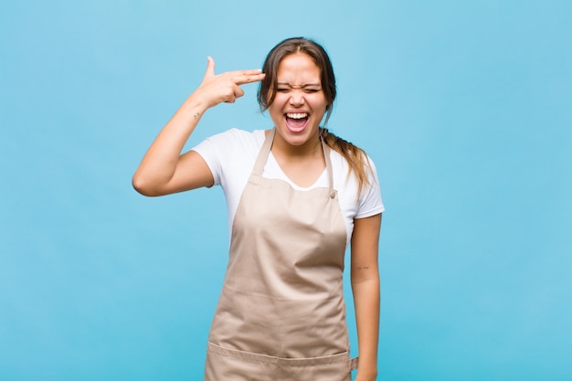 Young hispanic woman looking unhappy and stressed, suicide gesture making gun sign with hand, pointing to head