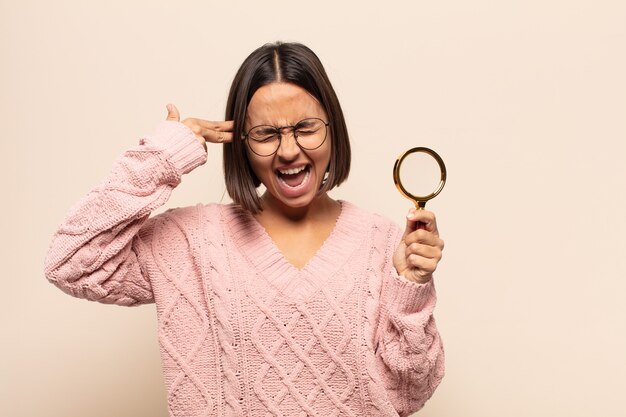 Young hispanic woman looking unhappy and stressed, suicide gesture making gun sign with hand, pointing to head