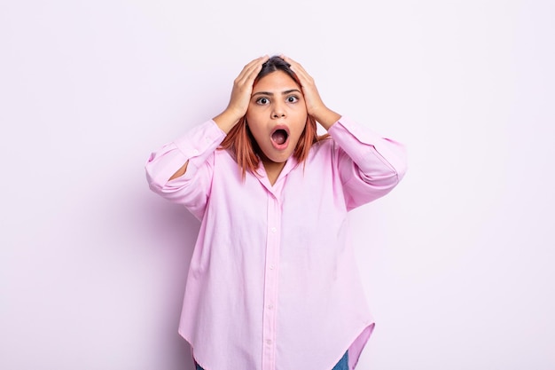 Young hispanic woman looking unpleasantly shocked, scared or worried, mouth wide open and covering both ears with hands