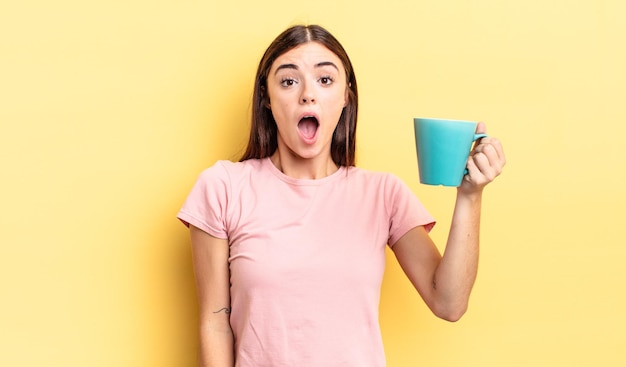 Photo young hispanic woman looking very shocked or surprised. coffee cup concept