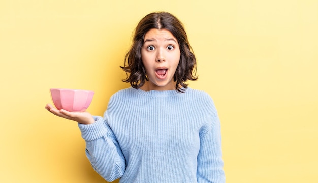 Young hispanic woman looking very shocked or surprised. empty bowl concept