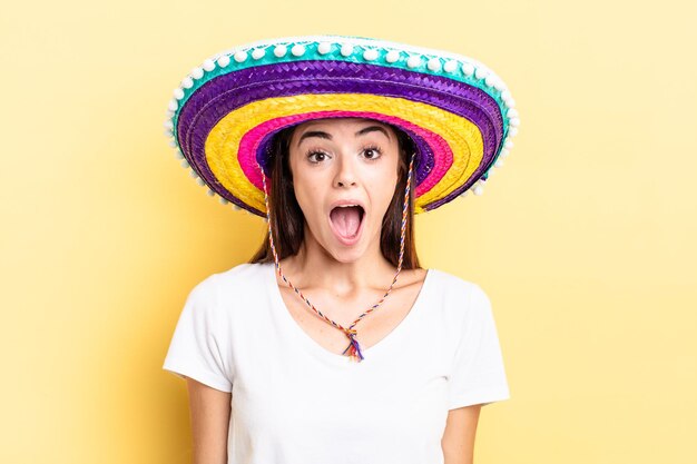 Young hispanic woman looking very shocked or surprised. mexican hat concept