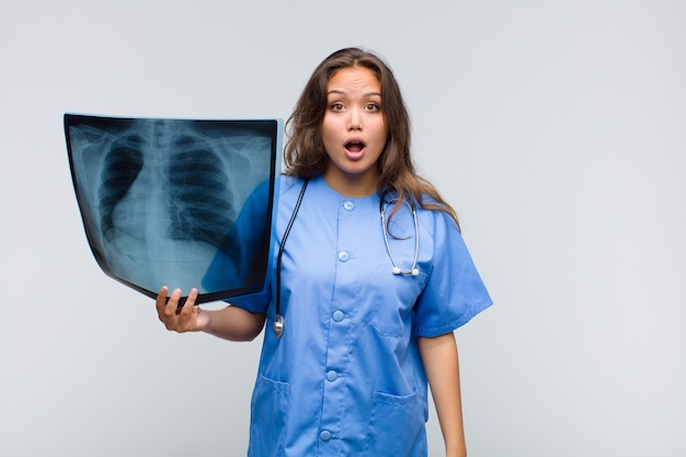 Young hispanic woman looking very shocked or surprised, staring with open mouth saying wow