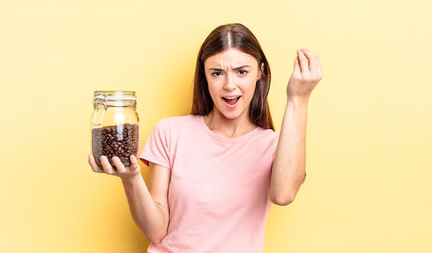 Young hispanic woman making capice or money gesture, telling you to pay. coffee beans concept