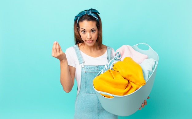 Young hispanic woman making capice or money gesture, telling you to pay and washing clothes