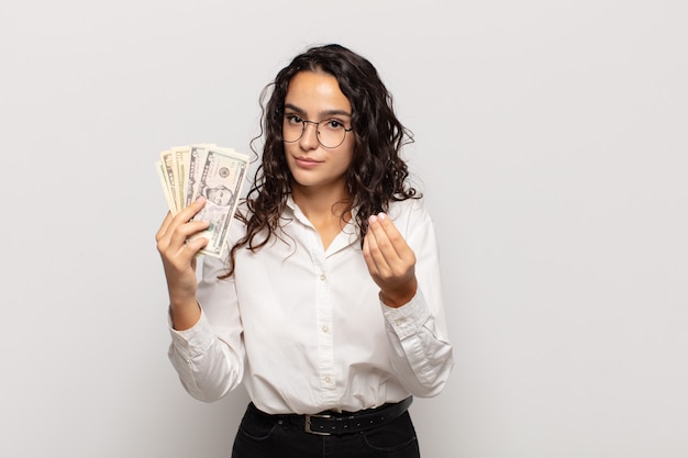 Young hispanic woman making capice or money gesture, telling you to pay your debts!