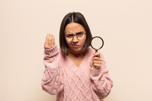 Young hispanic woman making capice or money gesture, telling you to pay your debts!