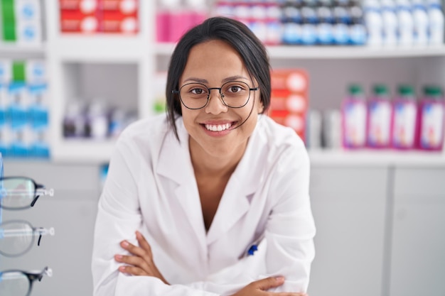 Young hispanic woman pharmacist smiling confident leaning on counter at pharmacy