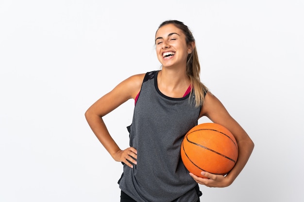 Young hispanic woman playing basketball over isolated white background posing with arms at hip and smiling