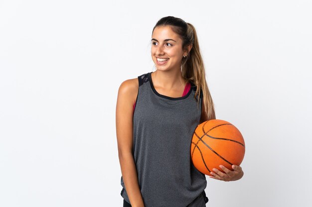 Young hispanic woman playing basketball over isolated white looking to the side and smiling