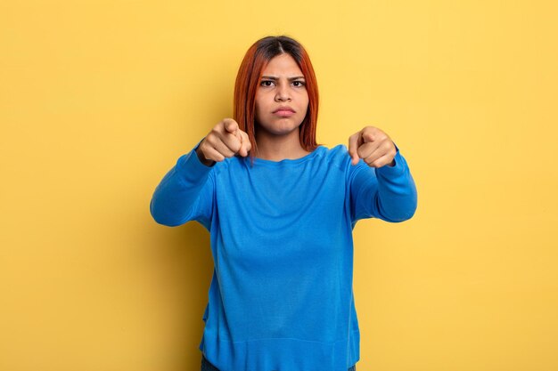 Young hispanic woman pointing forward at camera with both fingers and angry expression, telling you to do your duty