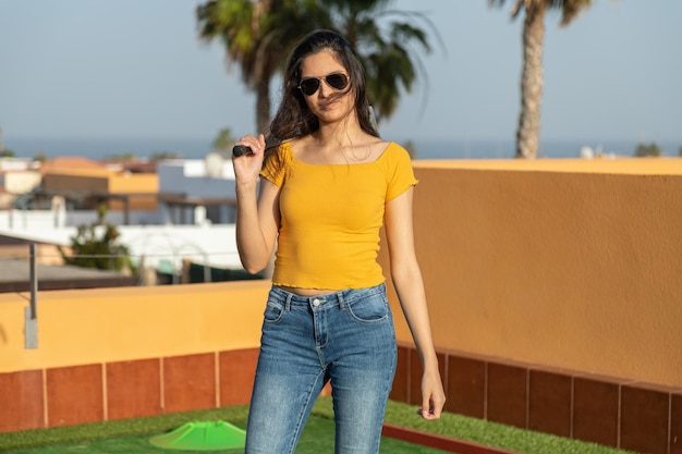 Photo young hispanic woman posing with a golf club playing miniature golf