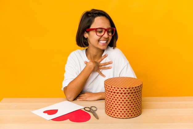 Young hispanic woman preparing a valentine gift isolated laughs out loudly keeping hand on chest.