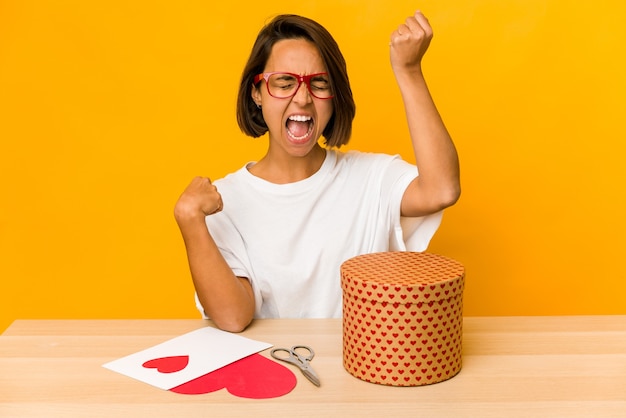 Young hispanic woman preparing a valentine gift isolated raising fist after a victory, winner concept.