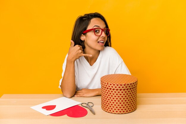 Young hispanic woman preparing a valentine gift isolated showing a mobile phone call gesture with fingers.