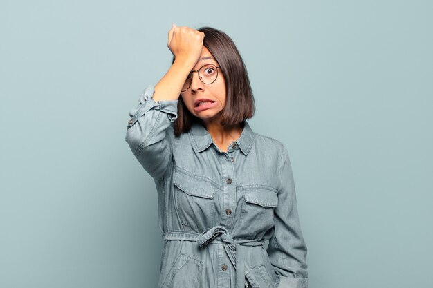 Young hispanic woman raising palm to forehead thinking oops, after making a stupid mistake or remembering, feeling dumb