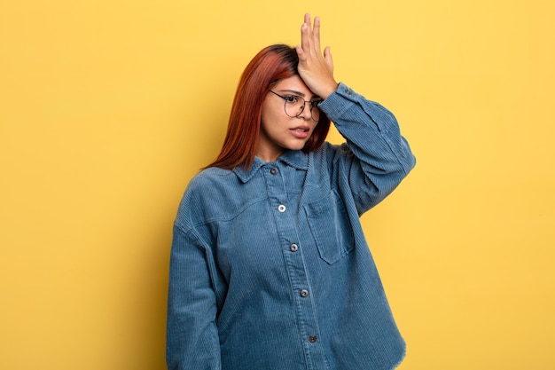 young hispanic woman raising palm to forehead thinking oops, after making a stupid mistake or remembering, feeling dumb