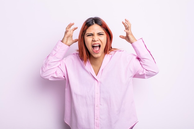 young hispanic woman screaming in panic or anger, shocked, terrified or furious, with hands next to head