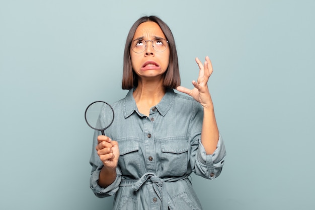 Young hispanic woman screaming with hands up in the air, feeling furious, frustrated, stressed and upset