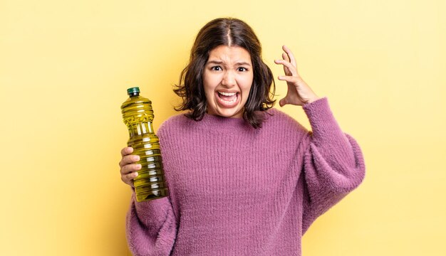 Young hispanic woman screaming with hands up in the air. olive oil concept