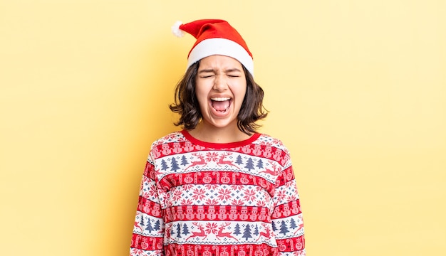 Young hispanic woman shouting aggressively, looking very angry. christmas concept