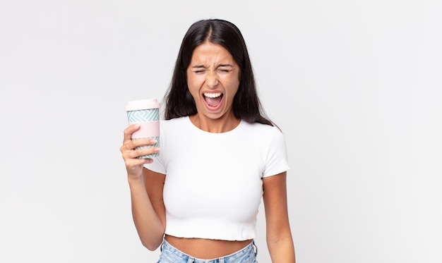 Young hispanic woman shouting aggressively, looking very angry and holding a take away coffee container