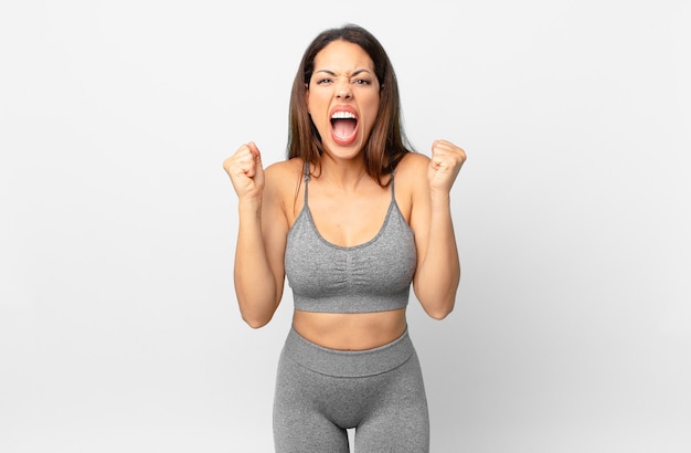 Young hispanic woman shouting aggressively with an angry expression. fitness concept