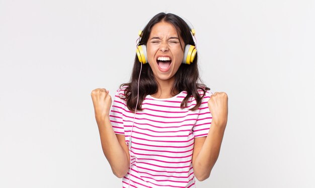 Young hispanic woman shouting aggressively with an angry expression listening music with headphones