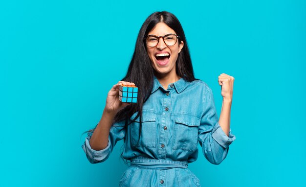 Young hispanic woman shouting aggressively with an angry expression or with fists clenched celebrating success. intelligence problem concept