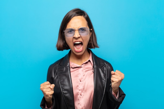 Young hispanic woman shouting aggressively with an angry expression or with fists clenched celebrating success