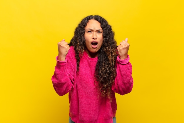 Young hispanic woman shouting aggressively with an angry expression or with fists clenched celebrating success