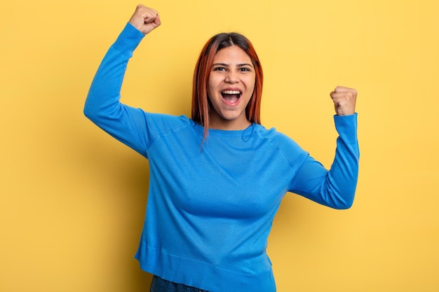 Young hispanic woman shouting triumphantly, looking like excited, happy and surprised winner, celebrating