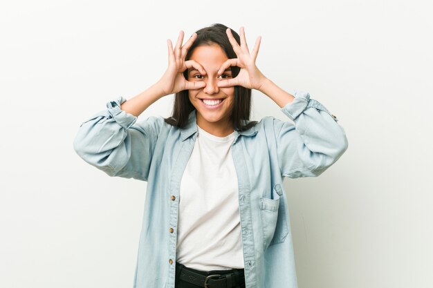 Young hispanic woman showing okay sign over eyes