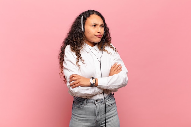 Young hispanic woman shrugging, feeling confused and uncertain, doubting with arms crossed and puzzled look. telemarketer concept