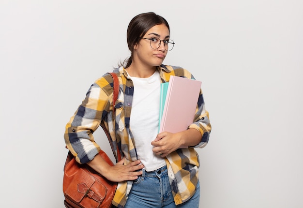 Young hispanic woman shrugging, feeling confused and uncertain, doubting with arms crossed and puzzled look