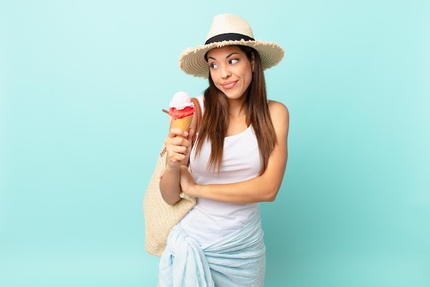 젊은 히스패닉계 여성이 어깨를 으쓱하고 혼란스럽고 불확실하다고 느끼며 아이스크림을 들고 있습니다. 여름 개념