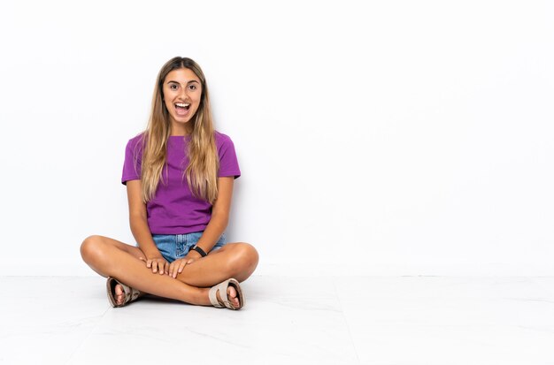 Young hispanic woman sitting on the floor with surprise facial expression