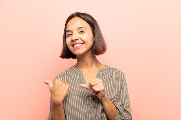 young hispanic woman smiling cheerfully and casually pointing to copy space on the side, feeling happy and satisfied