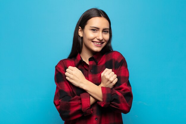 Young hispanic woman smiling cheerfully and celebrating, with fists clenched and arms crossed, feeling happy and positive