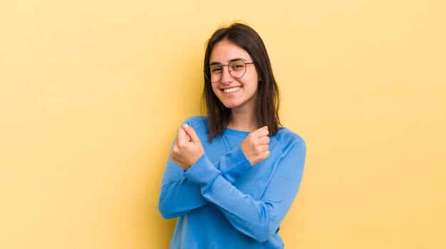 Young hispanic woman smiling cheerfully and celebrating with fists clenched and arms crossed feeling happy and positive