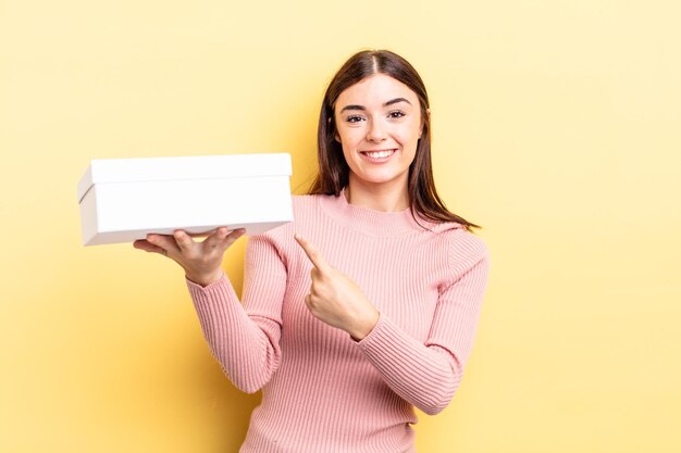 Young hispanic woman smiling cheerfully, feeling happy and pointing to the side. empty box concept