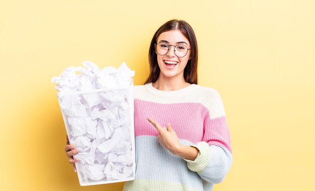 Young hispanic woman smiling cheerfully, feeling happy and pointing to the side. failure trash concept