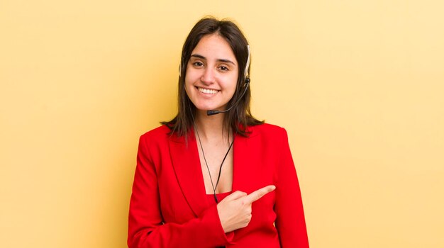 Young hispanic woman smiling cheerfully feeling happy and pointing to the side telemarketer concept