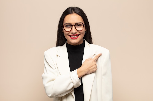 Young hispanic woman smiling cheerfully, feeling happy and pointing to the side and upwards, showing object in copy space