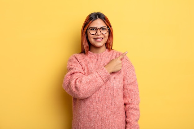 Young hispanic woman smiling cheerfully, feeling happy and pointing to the side and upwards, showing object in copy space