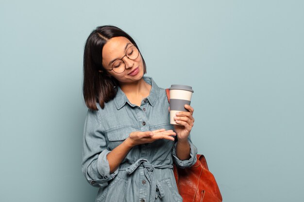 Young hispanic woman smiling cheerfully, feeling happy and showing a concept in copy space with palm of hand