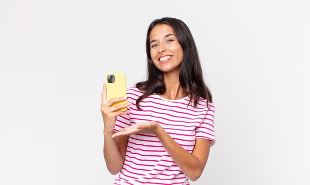 Young hispanic woman smiling cheerfully, feeling happy and showing a concept and holding a smartphone