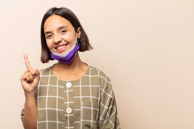 Young hispanic woman smiling cheerfully and happily, pointing upwards with one hand to copy space